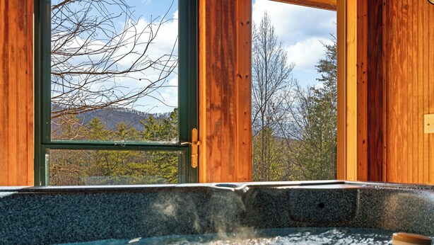 A wooden cabin with a hot tub and a view of trees and mountains. - This cabin is a 3 bedroom(s), 1 bathrooms, located in Sevierville, TN. (Sevierville)
