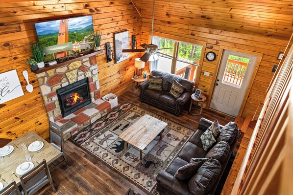 A cozy cabin interior with a stone fireplace, wooden walls, a leather sofa, and a dining area.