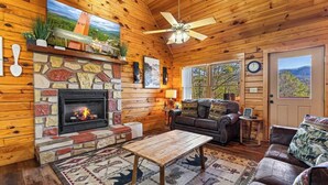 A cozy cabin interior with a stone fireplace, wooden walls, a leather sofa, and a dining table. - This cabin is a 3 bedroom(s), 1 bathrooms, located in Sevierville, TN. (Sevierville)