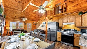 A wooden cabin with a dining area, kitchen, and a staircase leading to a loft. - This cabin is a 3 bedroom(s), 1 bathrooms, located in Sevierville, TN. (Sevierville)