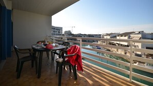 A balcony with a table and chairs, overlooking a marina with boats and buildings. - Flat with terrace near the beach (Lignano Sabbiadoro)
