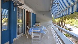 A balcony with a table and chairs, a blue awning, and a view of the street. - Cozy flat near the sea in Lignano Sabbiadoro (Lignano Sabbiadoro)