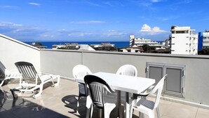 A rooftop terrace with a table and chairs, a view of the sea, and modern buildings in the background. - Apartment with solarium in Lignano (Lignano Sabbiadoro)