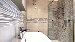 Une salle de bain moderne avec une grande baignoire, une douche dotée d’une porte en verre et un mur orné de carreaux à rayures.