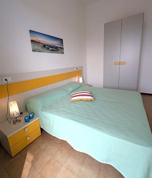 A bedroom with a bed, a nightstand, a bedside lamp, a picture on the wall, and a wardrobe.