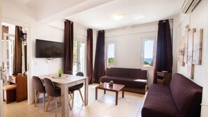 Una sala de estar moderna con comedor, sofá, televisor y vistas al exterior.