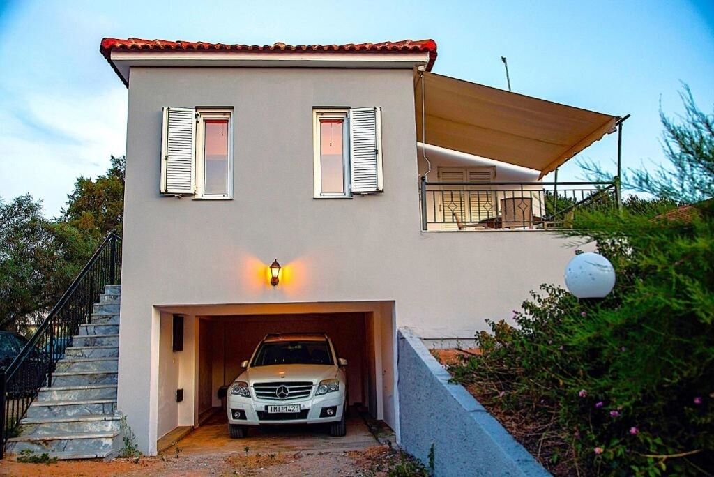 Ett modernt hus i två våningar med en bil parkerad i garaget, en trappa som leder till entrén och en täckt uteplats med sittplatser.