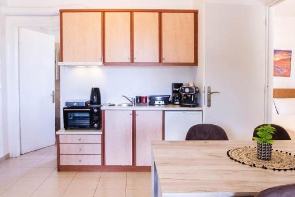 A compact kitchen with wooden cabinets, a microwave, a coffee maker, and a dining table with a placemat and a potted plant.
