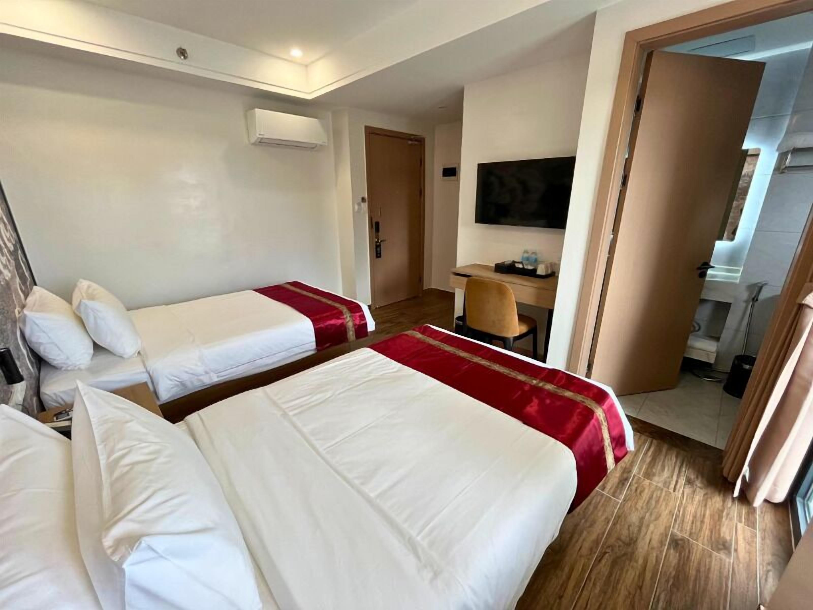 A hotel room with two beds, a desk, a TV, and a bathroom visible through an open door.