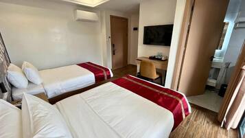A hotel room with two beds, a desk, a TV, and a bathroom visible through an open door.