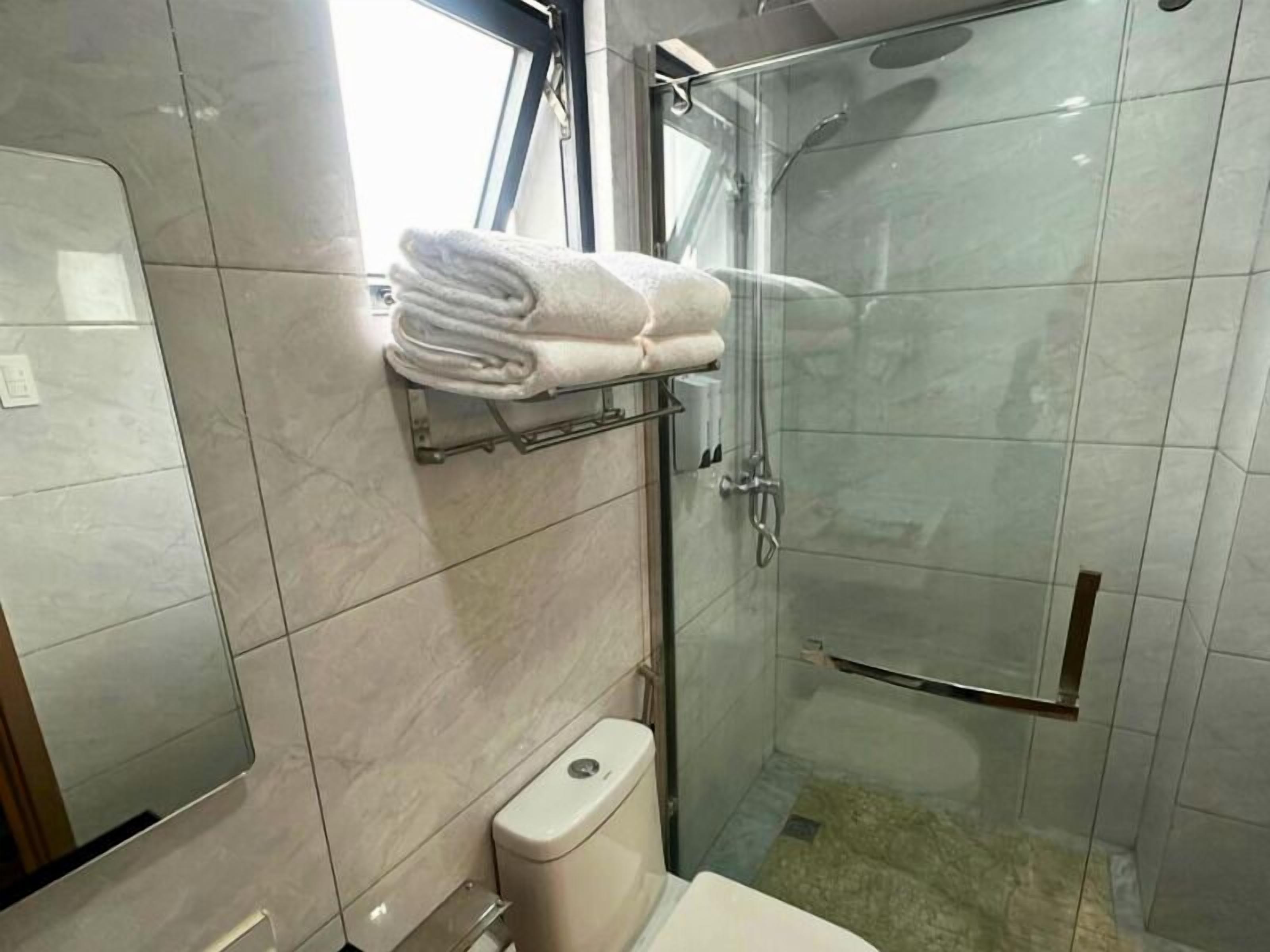 Un baño moderno con cabina de ducha de vidrio, un inodoro y un perchero con toallas dobladas.