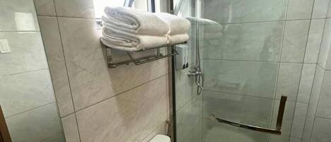 Un baño moderno con cabina de ducha de vidrio, un inodoro y un perchero con toallas dobladas.