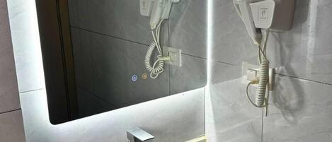 A bathroom with a large mirror, a hairdryer, and a sink with a faucet.