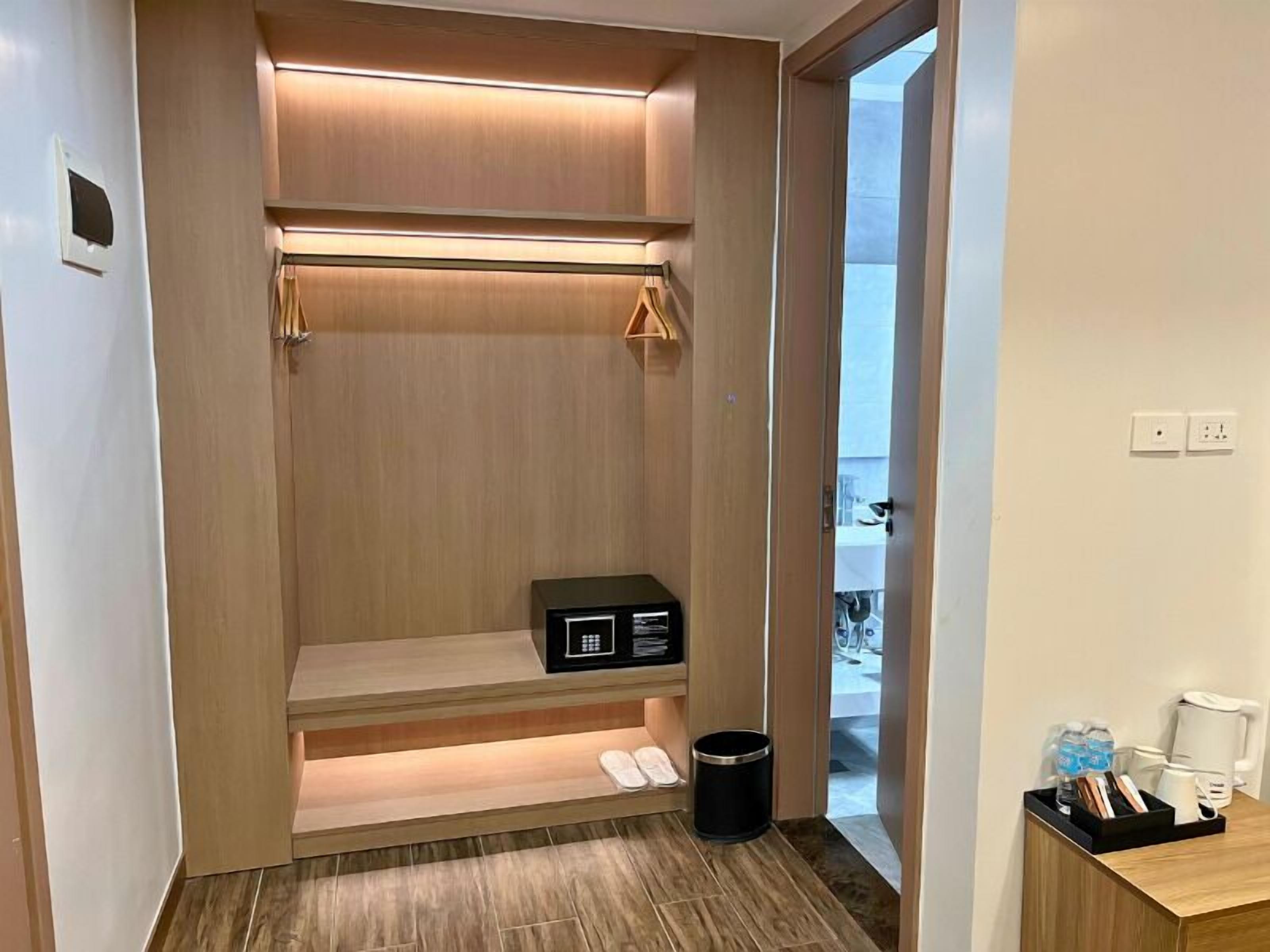 Un vestidor con estantes de madera, una caja de almacenamiento negra y un cubo de basura.
