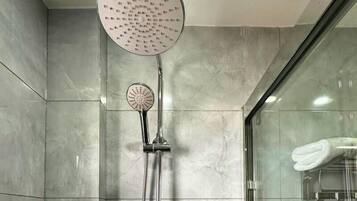 Un baño moderno con cabina de ducha de vidrio, ducha de mano y panel de control en la pared.
