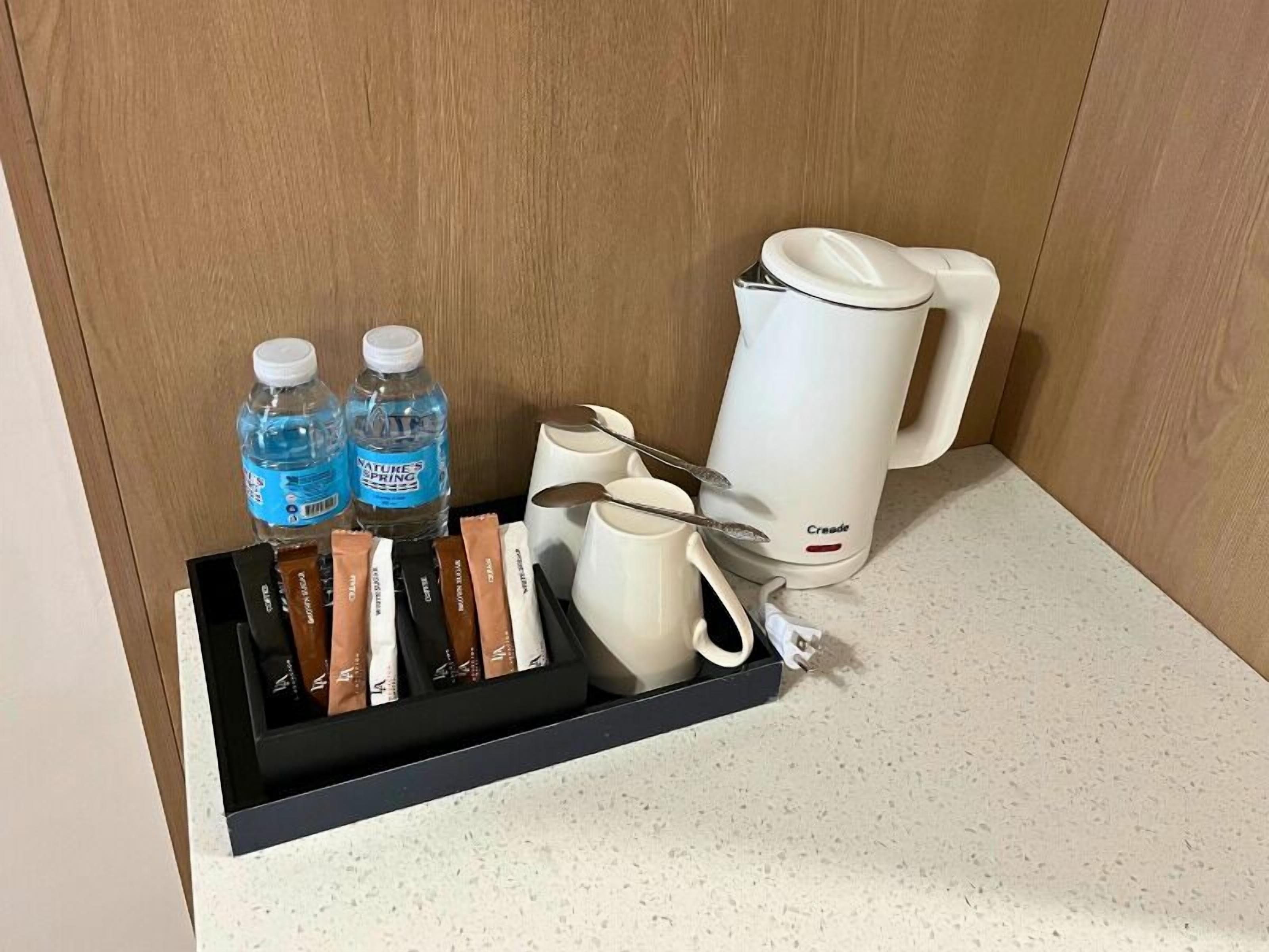 Et hotelminibar med vand på flaske, kaffekapsler, en kaffemaskine og et sæt skeer.