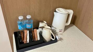 Minibar de hotel con agua embotellada, cápsulas de café, cafetera y juego de cucharas.