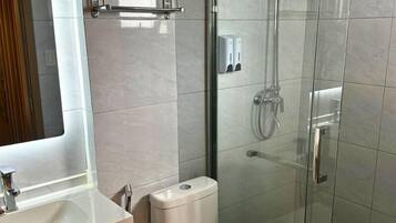Ein modernes Badezimmer mit Duschkabine aus Glas, Toilette, Waschbecken und Handtuchhalter.