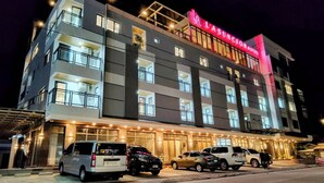 Un hôtel à plusieurs étages, reconnaissable à son grand panneau rouge, doté de nombreux balcons et disposant d’un parking où sont stationnées plusieurs voitures.