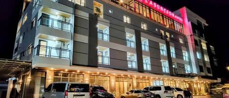 Un hôtel à plusieurs étages, reconnaissable à son grand panneau rouge, doté de nombreux balcons et disposant d’un parking où sont stationnées plusieurs voitures.
