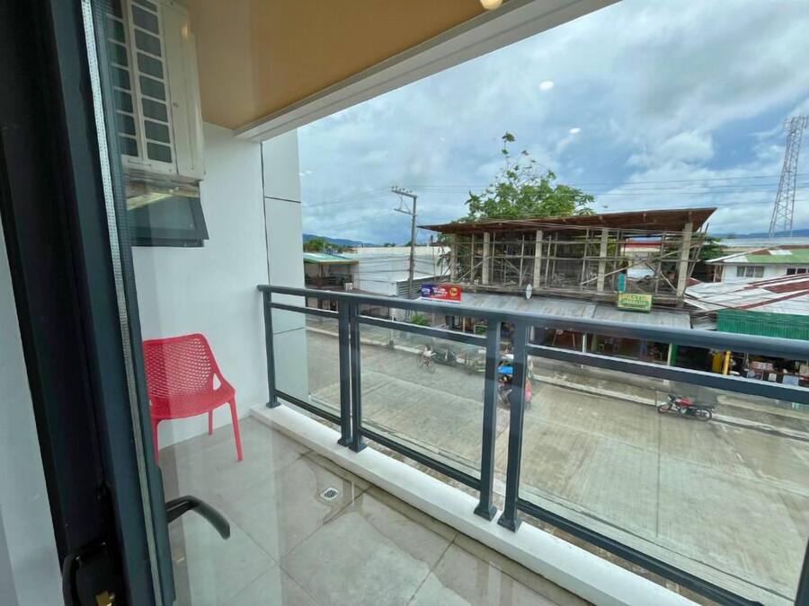 A balcony with a red chair, a view of a street with a building under construction, and a clear sky.