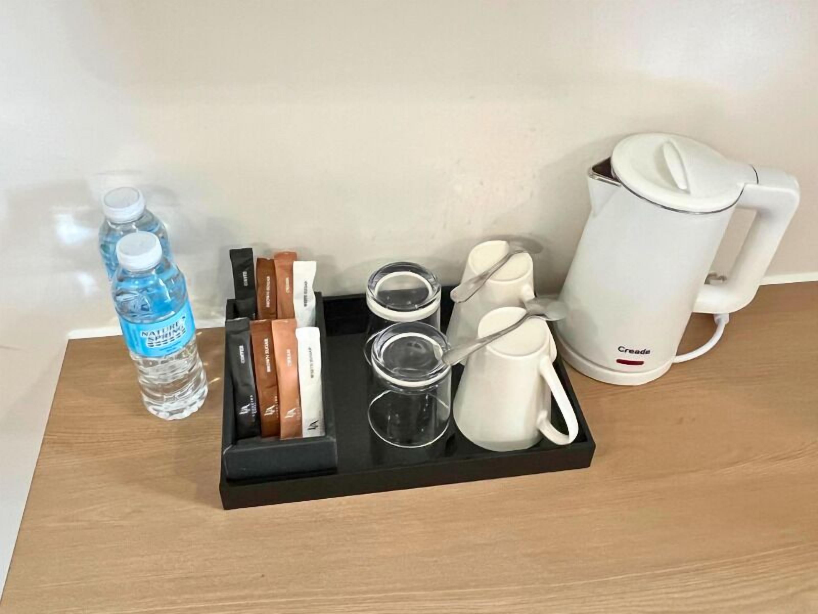 A tray with a water bottle, tea bags, a teapot, and cups on a wooden surface.