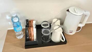 A tray with a water bottle, tea bags, a teapot, and cups on a wooden surface.