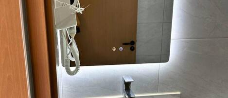 A bathroom with a white sink, a mirror, and a telephone mounted on the wall.