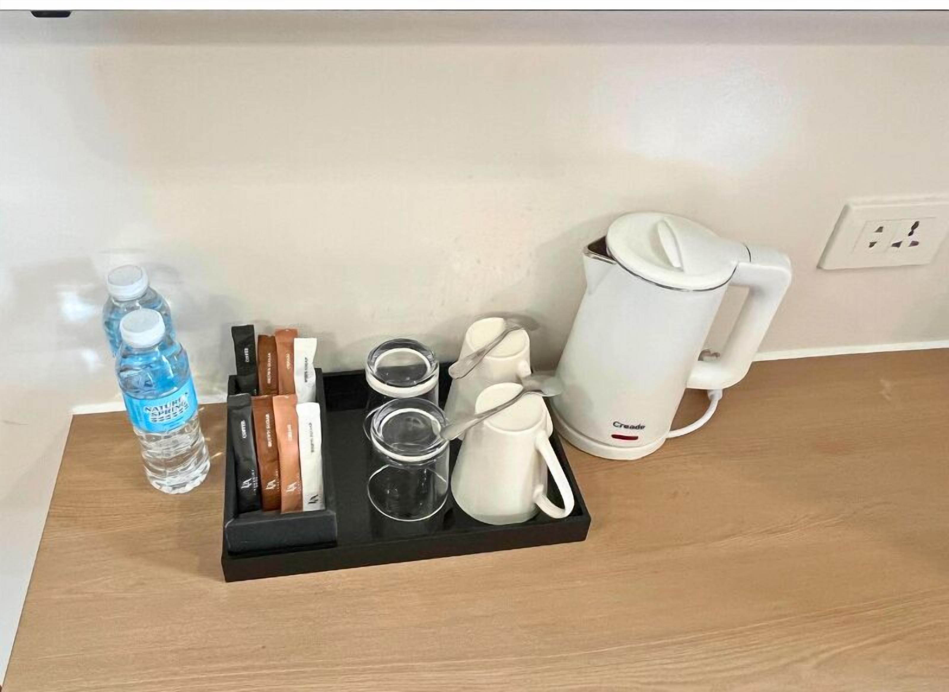 A tray with a water bottle, tea bags, glasses, and a coffee maker on a wooden surface.