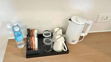 A tray with a water bottle, tea bags, glasses, and a coffee maker on a wooden surface.