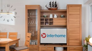 A modern living room with a wooden TV stand, a dining area with a table and chairs, and a decorative ship model. - Beautiful apartment for 4 guests with WIFI, TV and balcony (Norden)