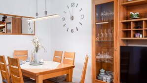 A dining area with a wooden table and chairs, a wall clock, and a cabinet with glassware. - Beautiful apartment for 4 guests with WIFI, TV and balcony (Norden)