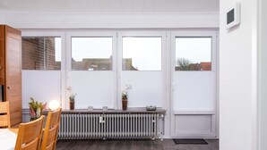 A room with a dining table, chairs, a radiator, and large windows with blinds. - Beautiful apartment for 4 guests with WIFI, TV and balcony (Norden)
