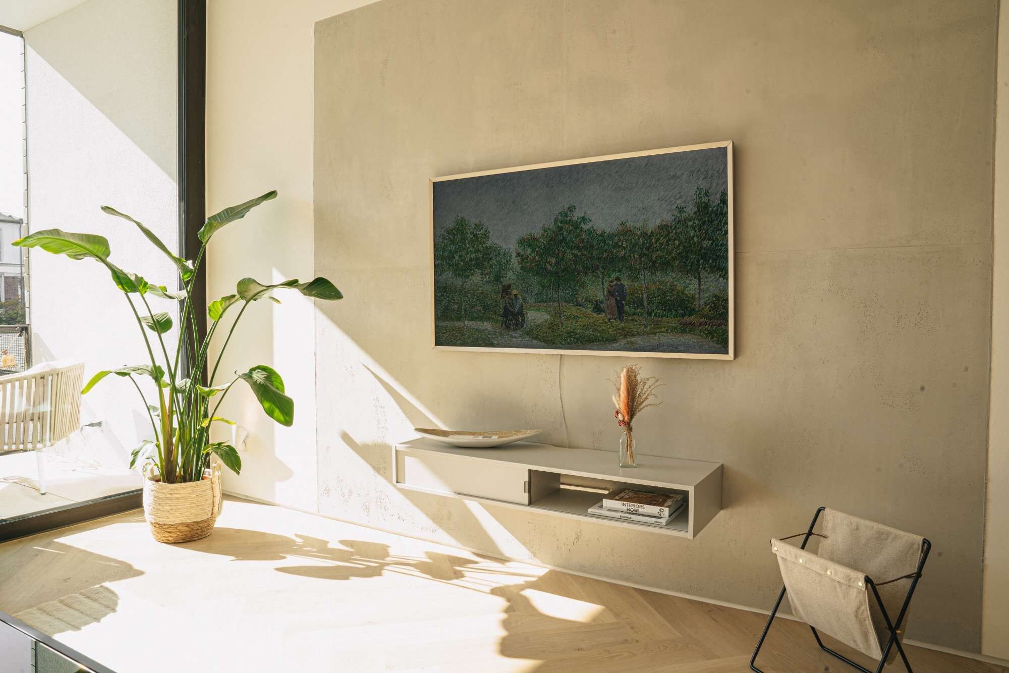 Una habitación con un ventanal grande, una planta en maceta, un cuadro, una mesita y una silla.