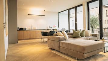 Un salon moderne doté d’un grand canapé d’angle, d’un coin repas avec une table et des chaises, et d’une cuisine avec des meubles en bois.