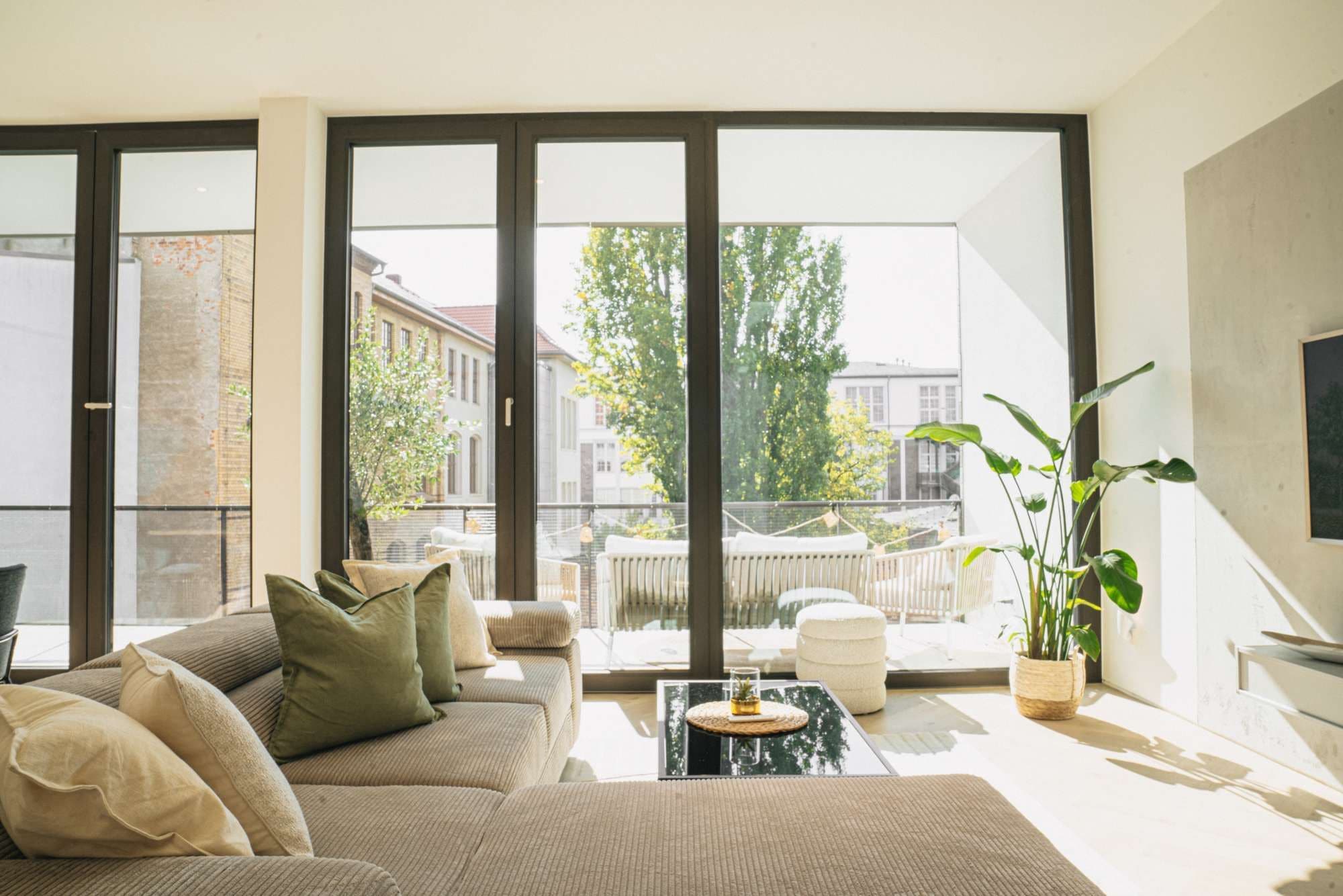 A modern living room with a sofa, a coffee table, and a large window offering a view of buildings and trees.