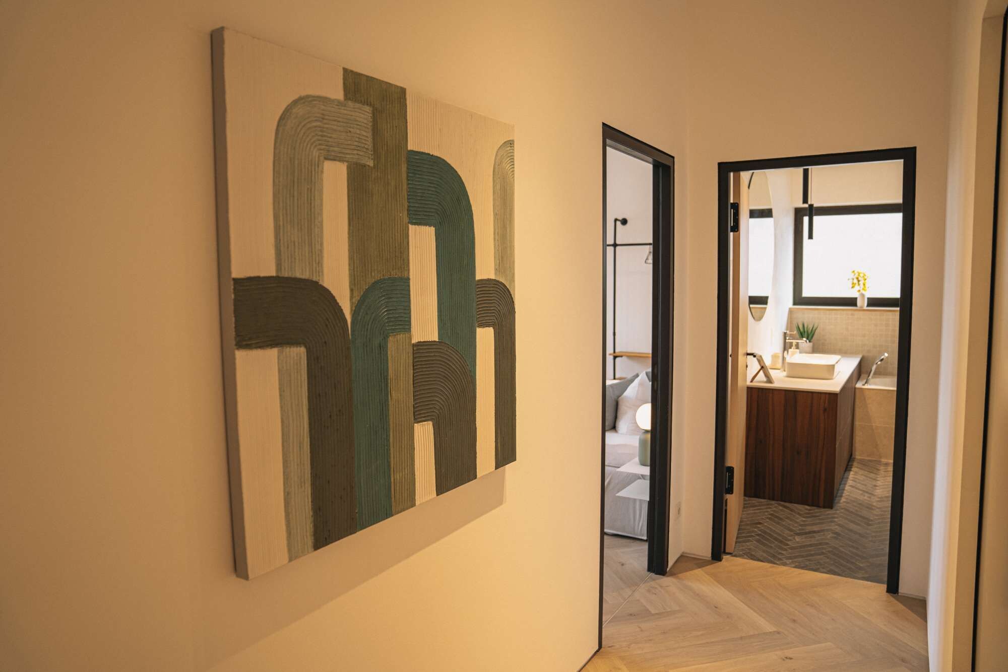 Ein Flur mit einem modernen, abstrakten Gemälde an der Wand, der zu einem Badezimmer mit Waschbecken und einer Topfpflanze führt.