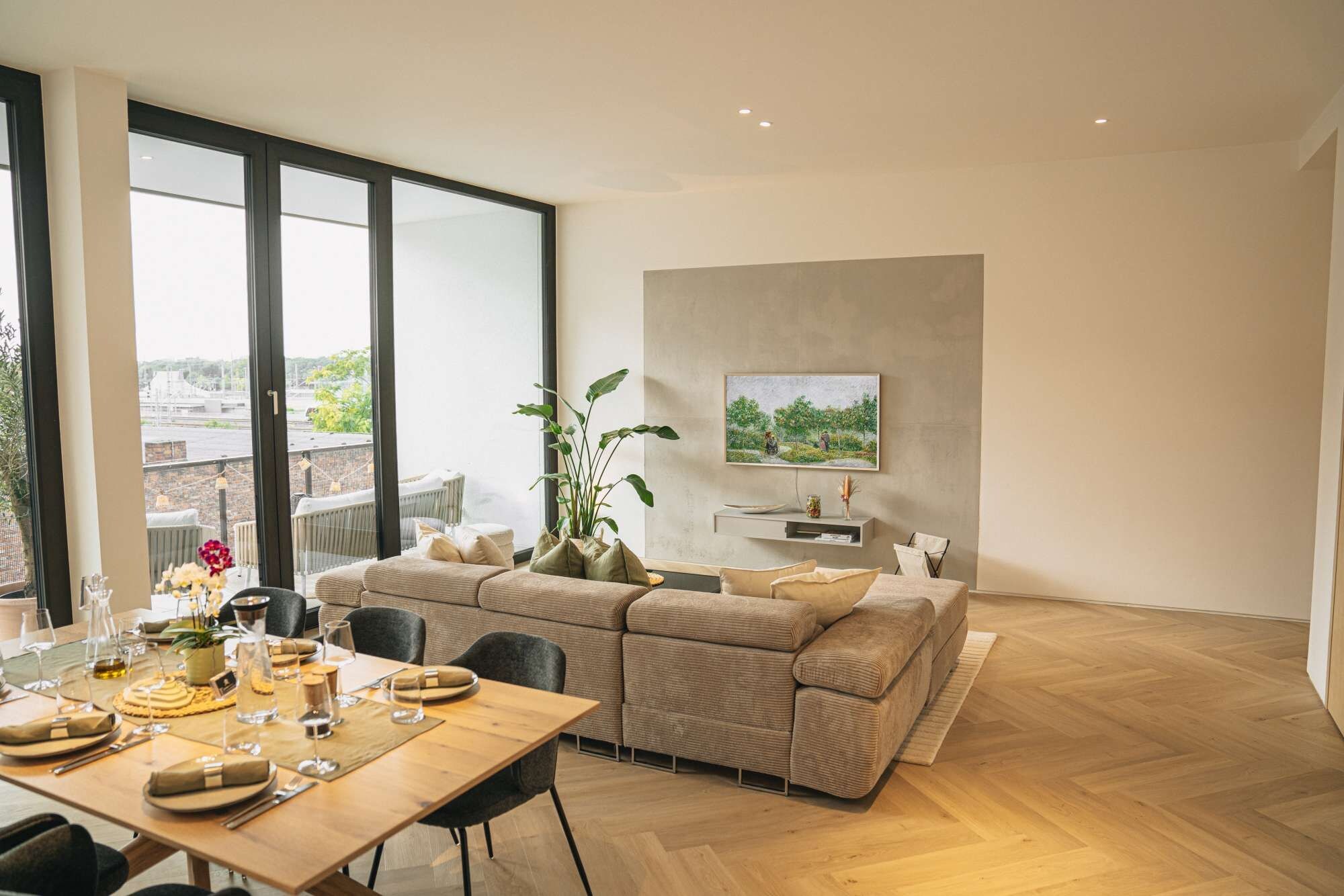 Un salon moderne avec un grand canapé, une table à manger dressée pour un repas et un téléviseur fixé au mur.