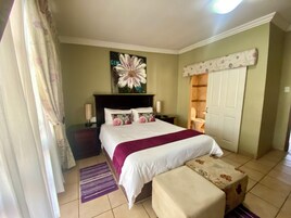 Un dormitorio con cama, mesita de noche, lámpara, cuadro, puerta y ventana con cortinas.