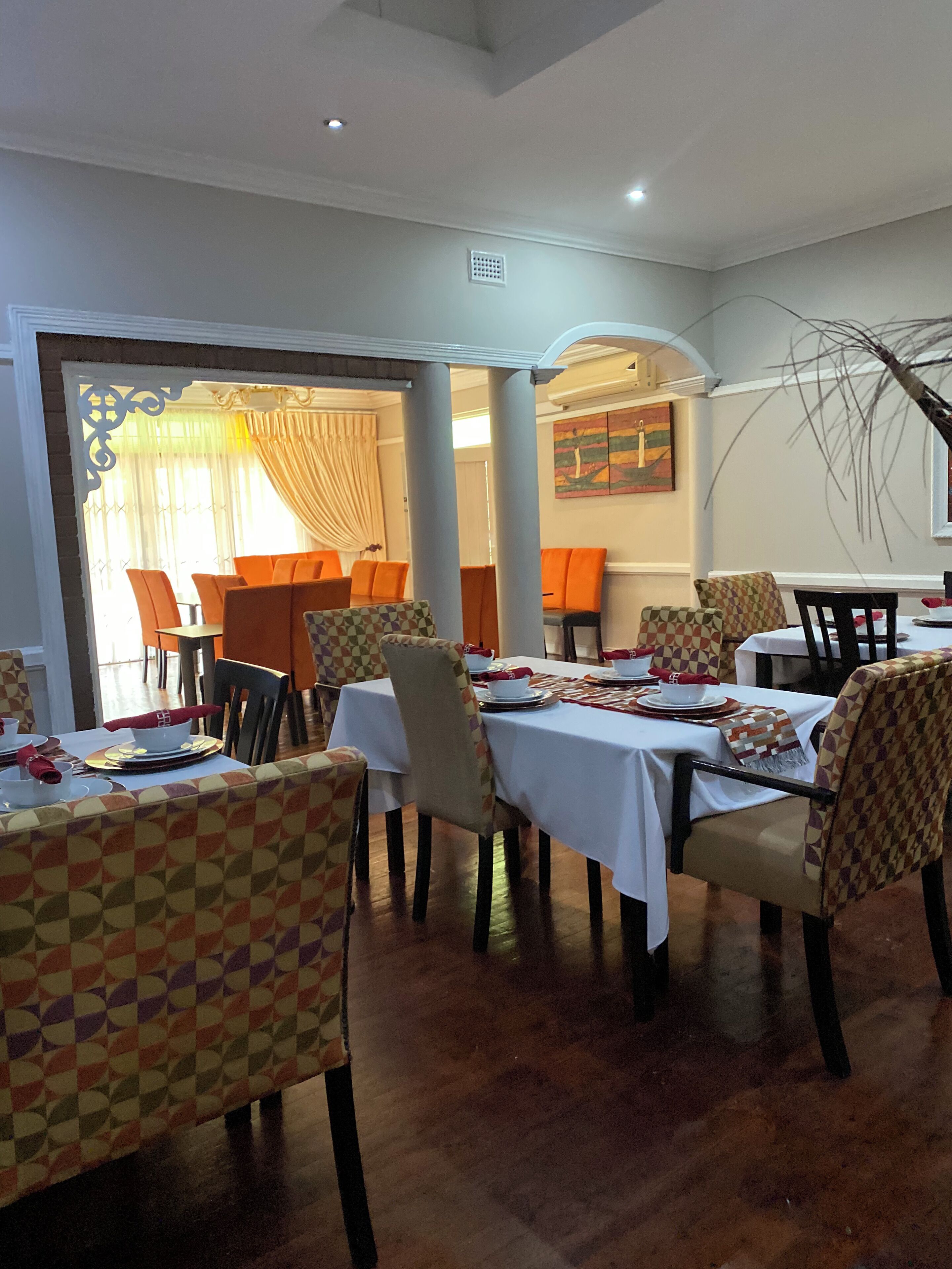 Un comedor con mesas dispuestas para cuatro, cada una con mantel estampado y sillas a juego. Hay dos puertas que conducen a otra habitación, una con cortina y la otra con puerta de cristal.