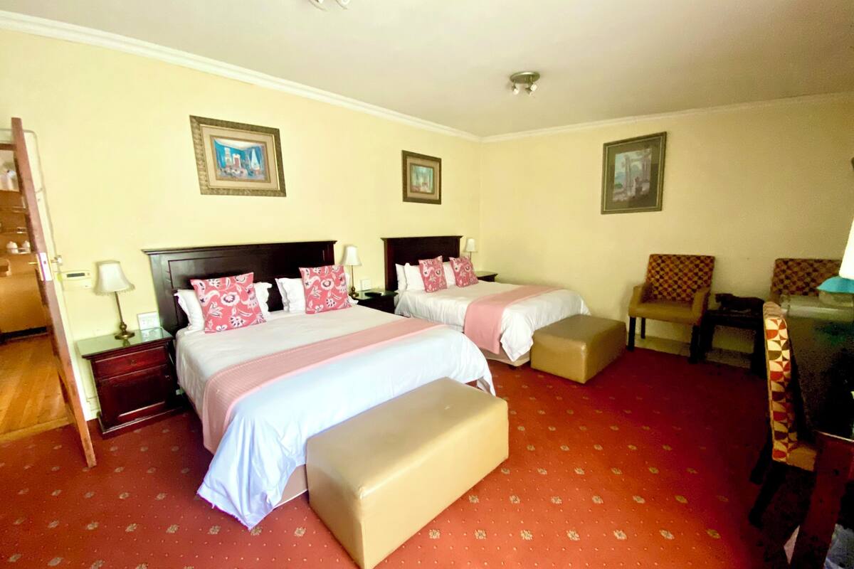 Een hotelkamer met twee bedden, een rood kleed en een houten vloer.