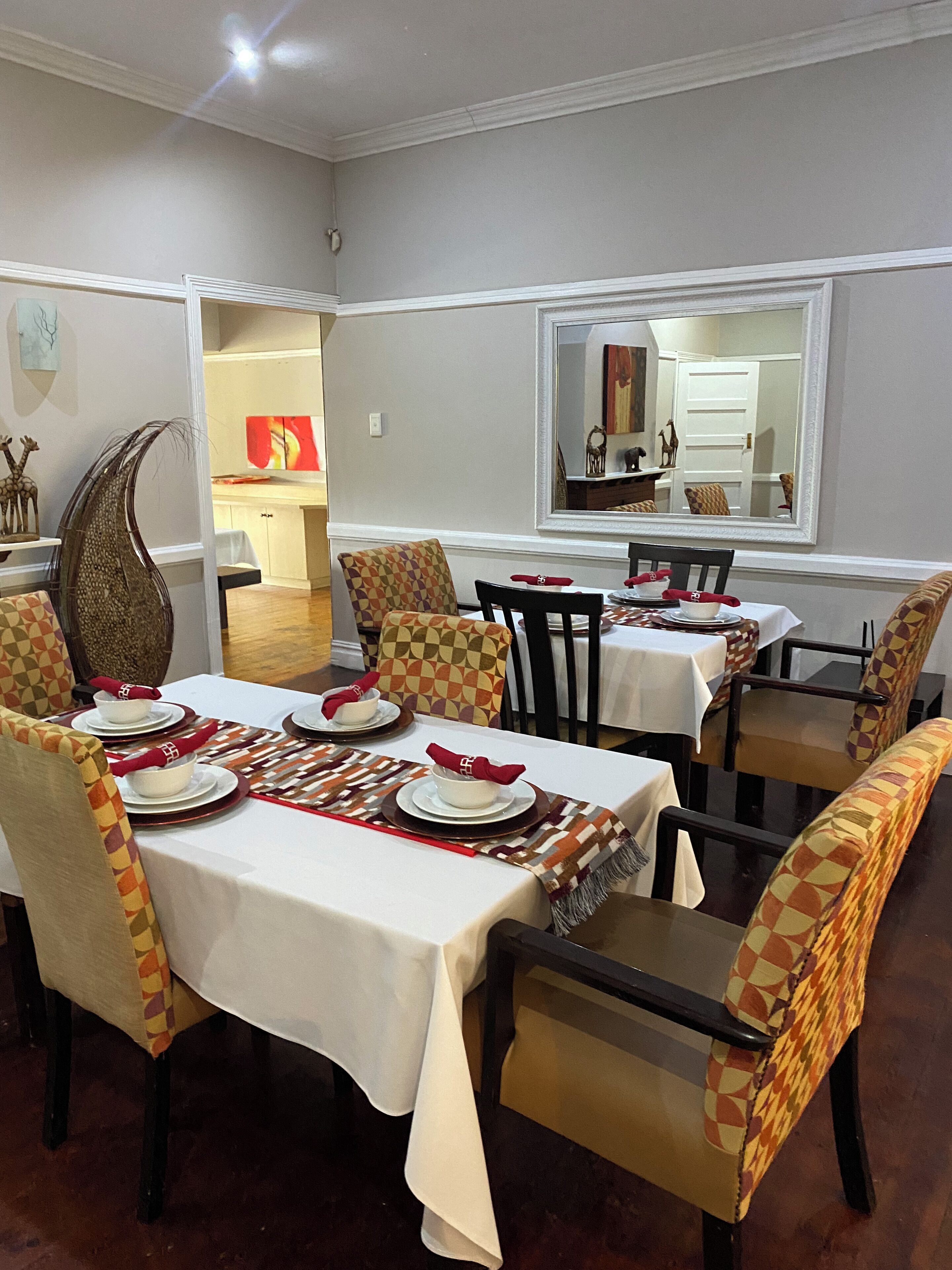 Un espace repas avec des tables dressées pour quatre personnes, chacune étant recouverte d’une nappe blanche et agrémentée de serviettes rouges. Les chaises sont à motifs à carreaux.