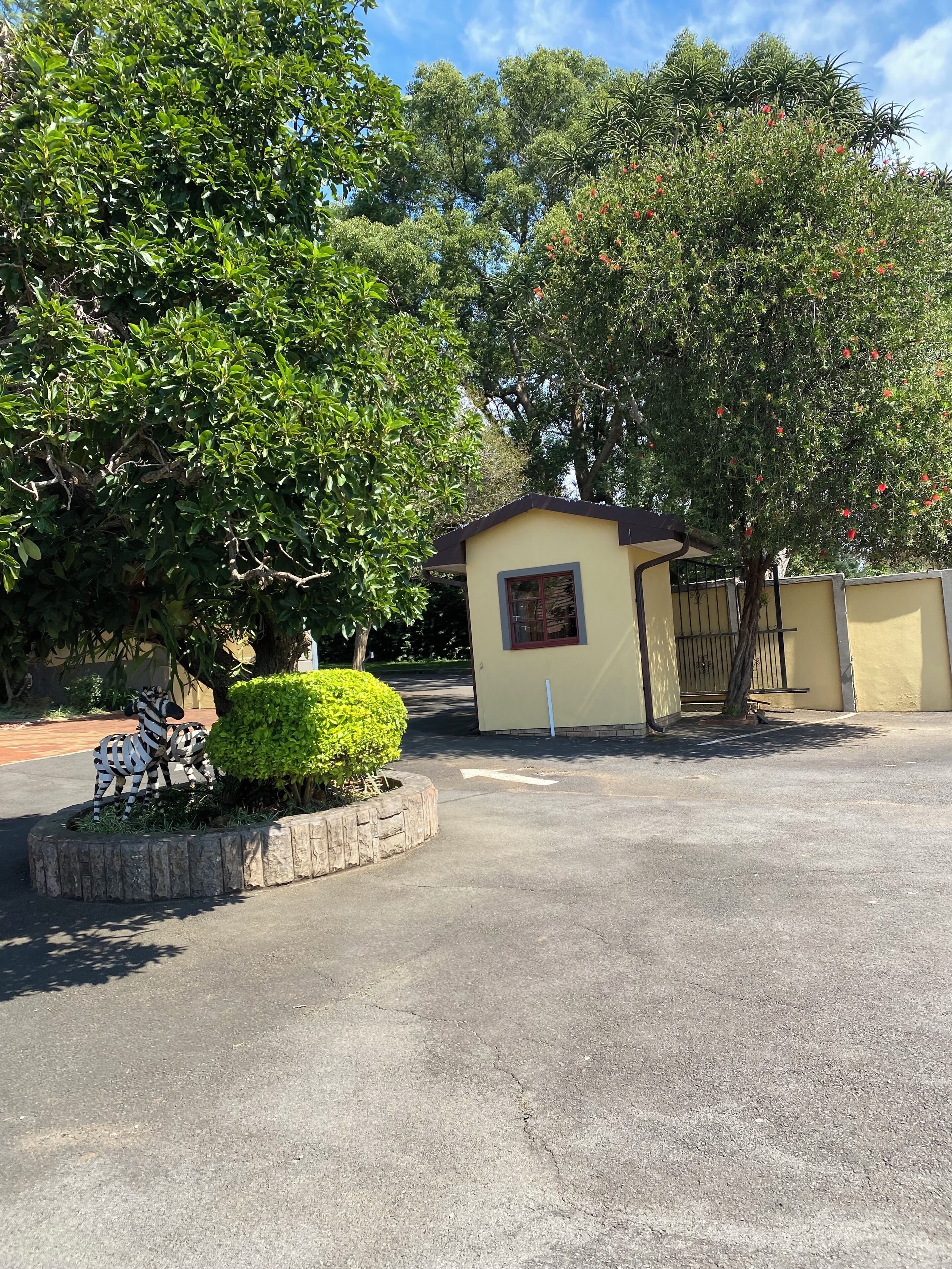 A parking area with a small building, surrounded by trees and a zebra statue.
