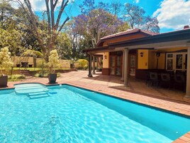 Una piscina con solárium empedrado, rodeada por un patio con mobiliario exterior y una zona cubierta.
