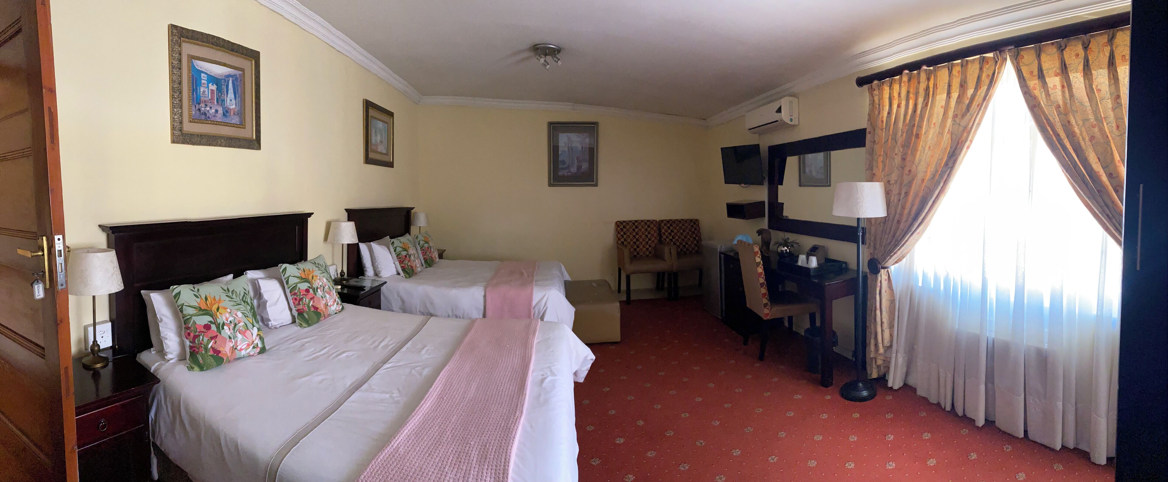 A hotel room with two beds, a desk, a chair, and a window with curtains.