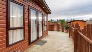 Een houten chalet met grote ramen, een houten terras en een omheind gebied.