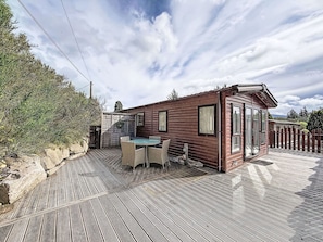 Une cabane en bois avec un patio, une table à manger et une petite terrasse.