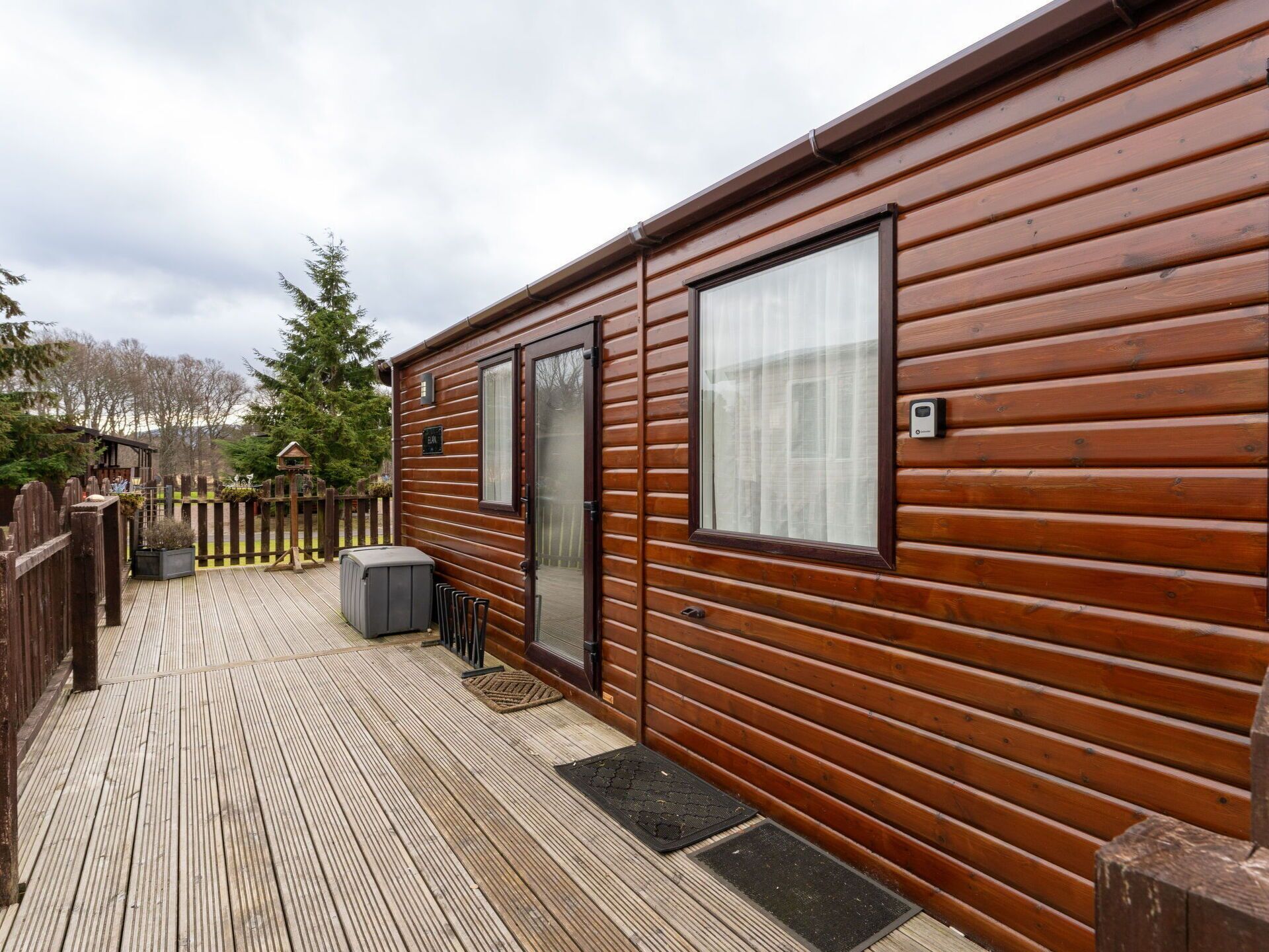 A wooden cabin with a deck, a door, and a window.