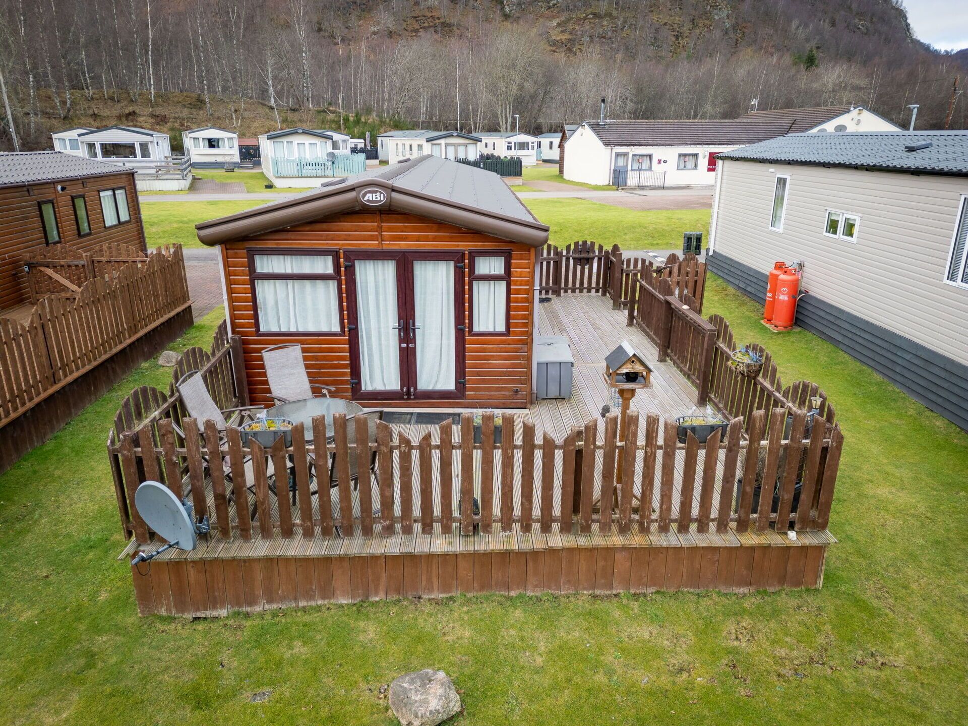 Eine Holzhütte mit eingezäunter Wiese, Satellitenschüssel und einer kleinen Terrasse.