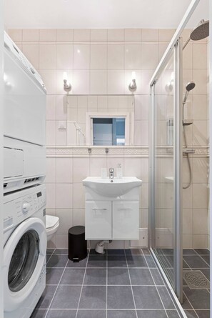 A modern bathroom with a washing machine, toilet, sink, and shower.